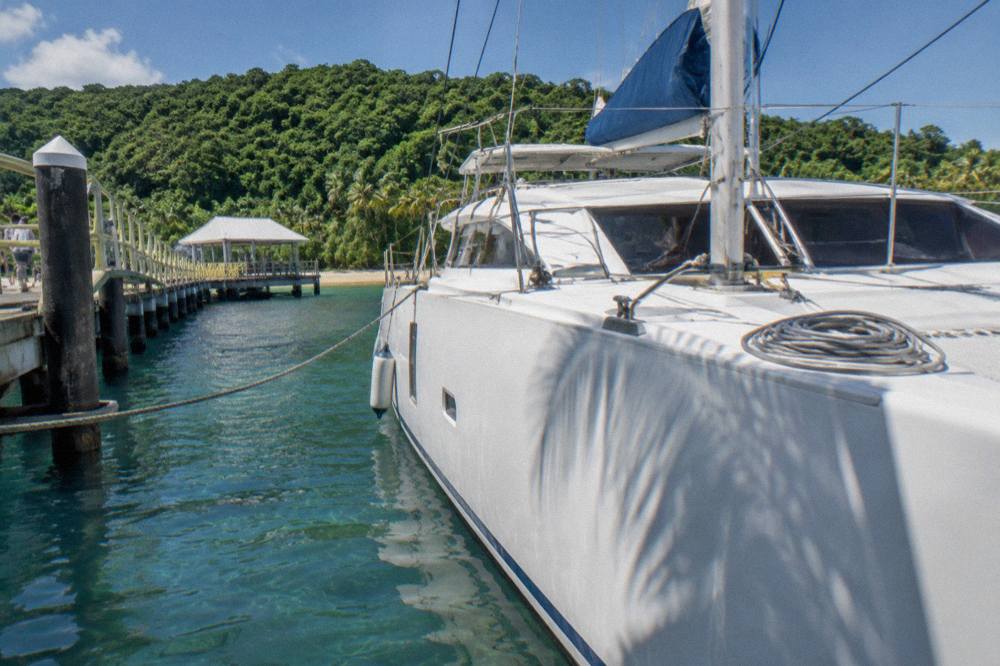 White catamaran moored at a tropical island jetty with rainforest behind