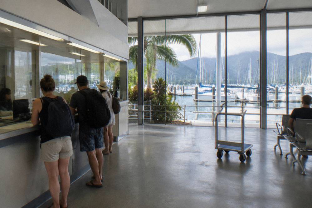 A ticket counter at a busy marina terminal with boats at berths behind glass