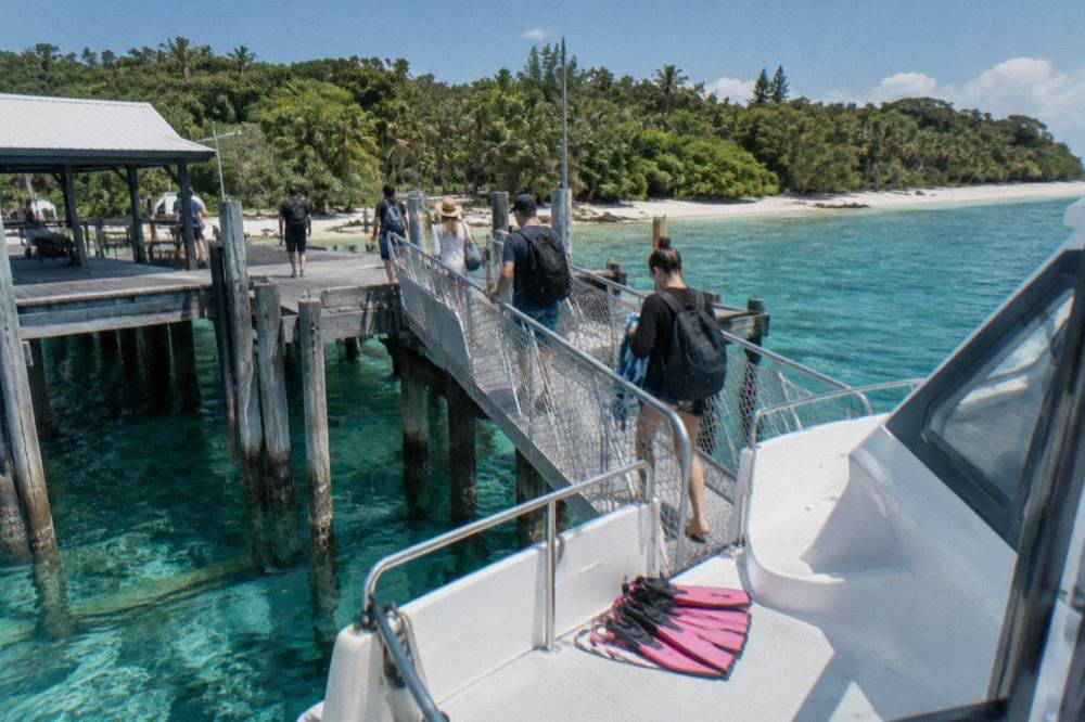 A white catamaran at an island jetty with passengers boarding down a gangplank