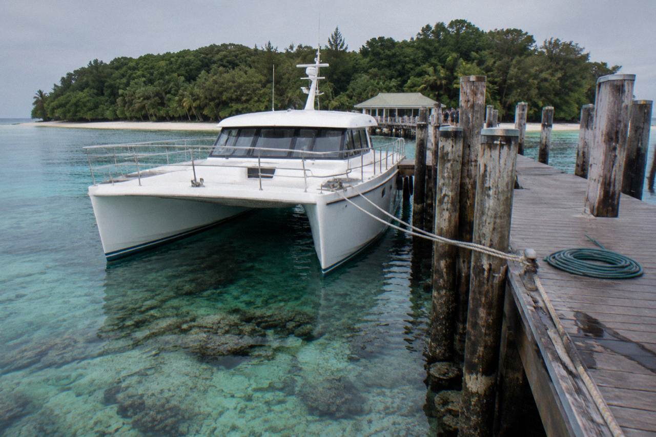 A catamaran moored at a tropical island jetty beside clear shallow reef water