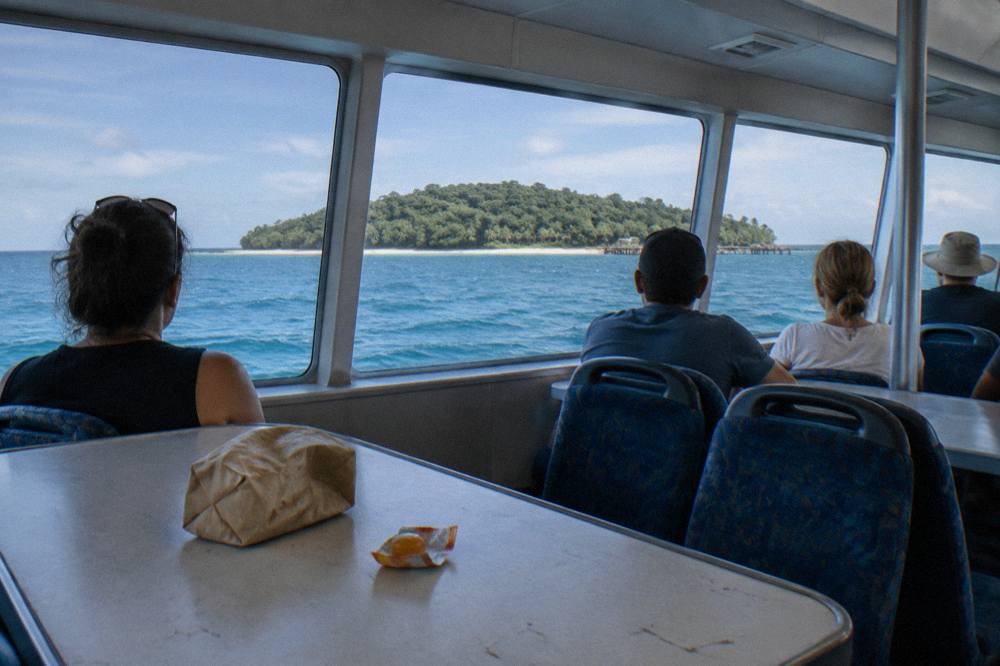 Passengers seated in the middle cabin of a catamaran looking out over open water toward a wooded island