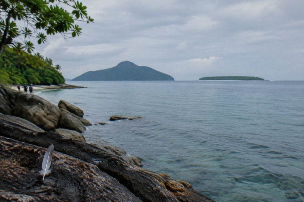 Two forested tropical islands seen across calm open water under a bright sky