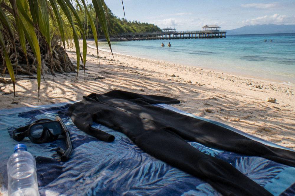 A full body lycra stinger suit laid out on a beach towel beside snorkel gear