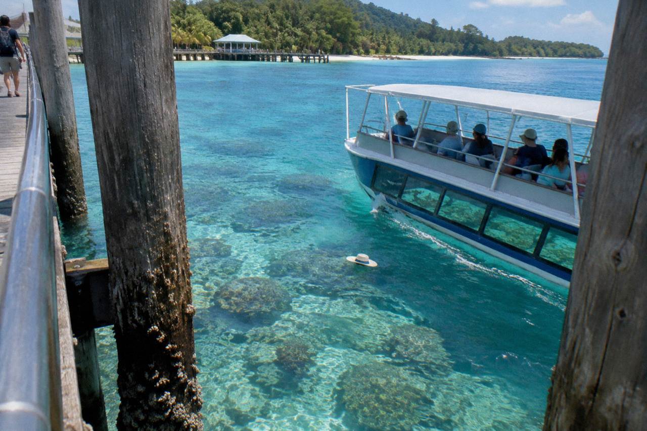 A glass bottom boat crossing clear turquoise water above coral near a tropical island