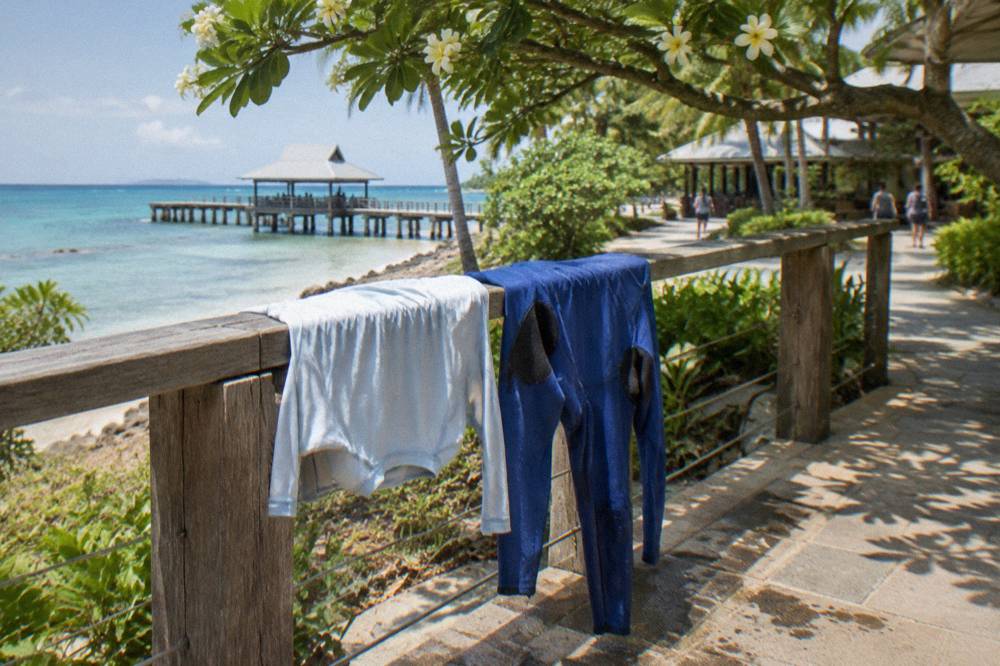 A rash vest and stinger suit drying on a railing in bright tropical sunlight