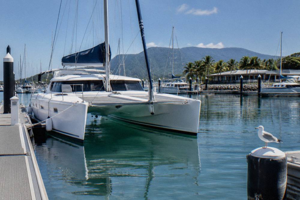 A sailing catamaran moored over clear reef water under a blue tropical sky
