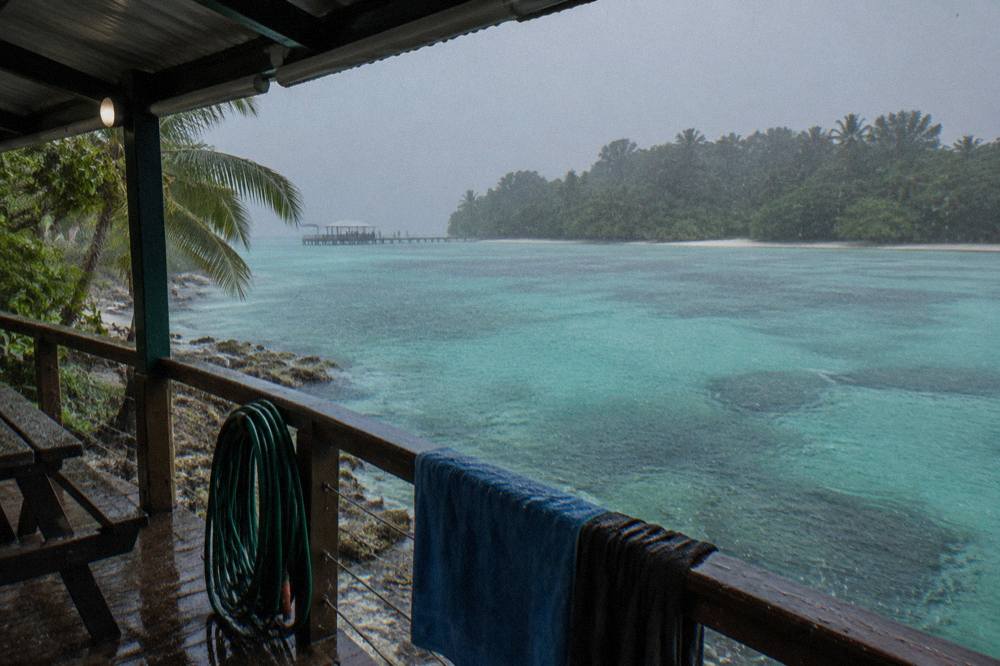 Heavy tropical rain falling on calm reef water near a covered boat deck