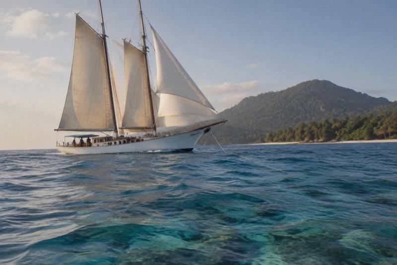 A schooner under sail on the Great Barrier Reef with Fitzroy Island granite headland on the horizon