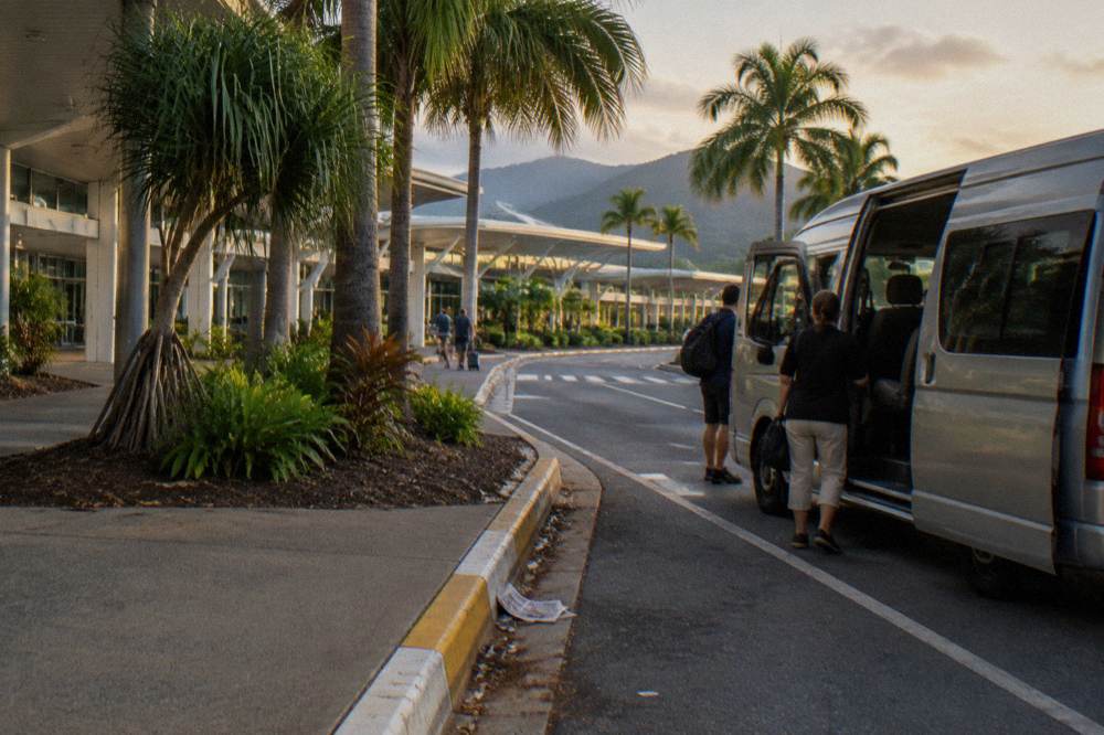 A taxi and shuttle bus lane outside a tropical airport terminal building