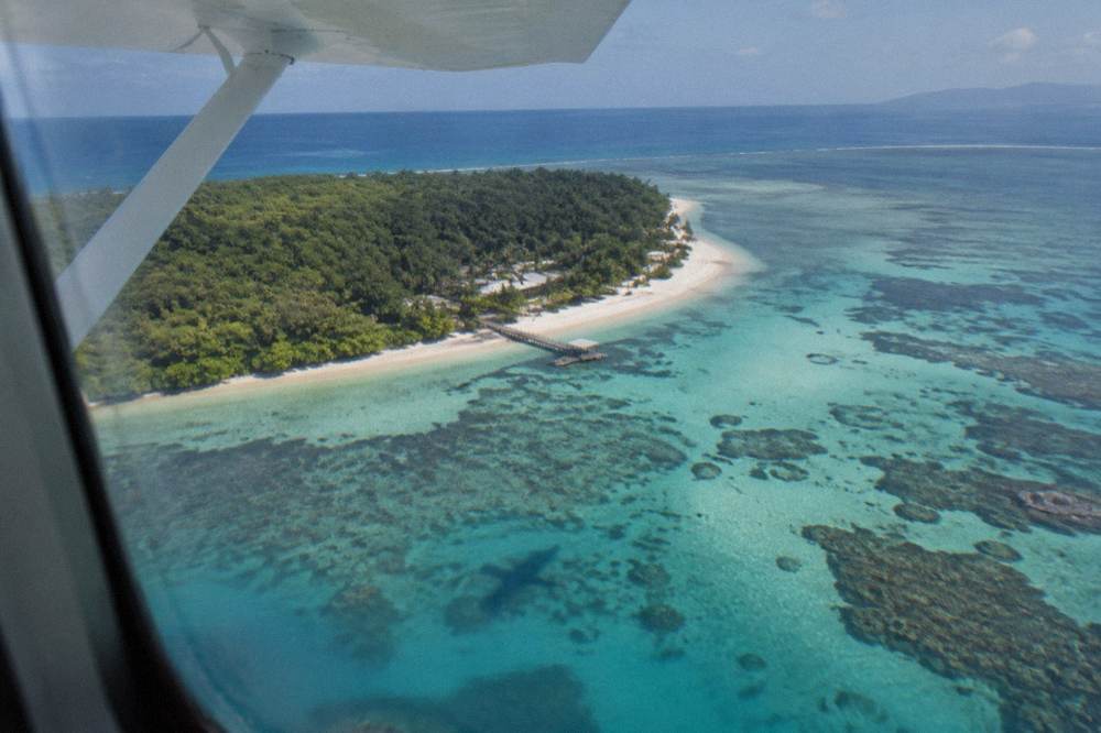 A light aircraft flying low over turquoise reef water and coral patterns