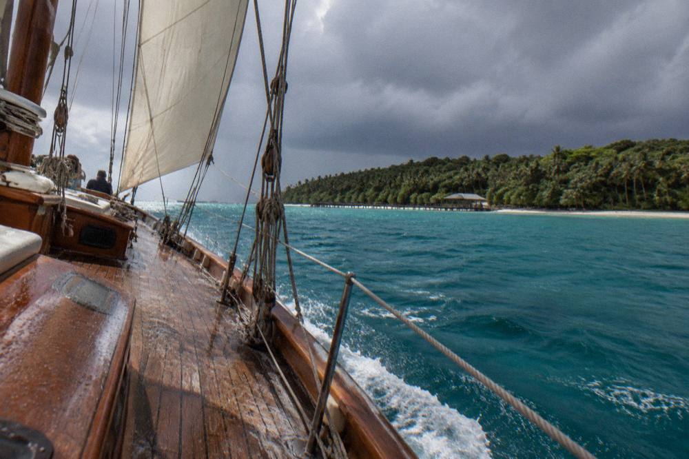 A sailing schooner under way on open water near a tropical coastline