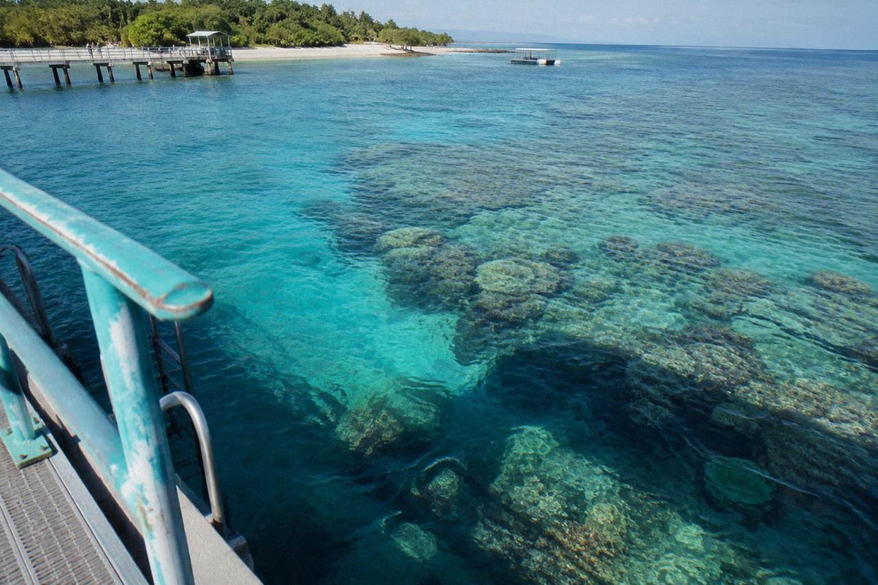 A white pontoon moored over clear reef water with coral visible below the surface