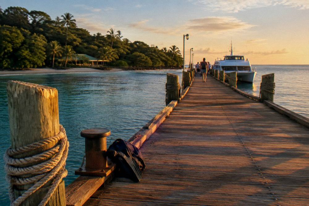 A jetty at golden hour with a catamaran waiting and calm water beyond
