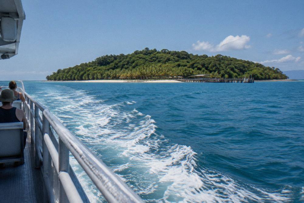 Fast catamaran ferry cruising across calm blue tropical water toward a green island