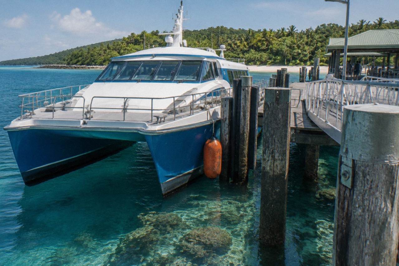Fast catamaran ferry moored at a tropical island jetty beside clear shallow reef water