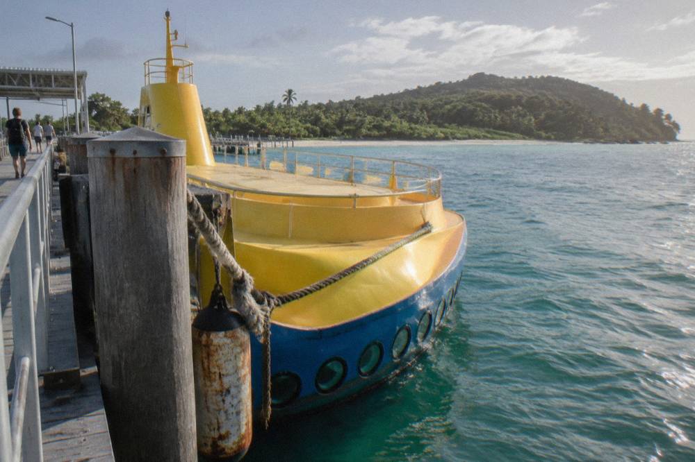 Semi-submarine vessel with below-deck porthole windows moored at a tropical island jetty
