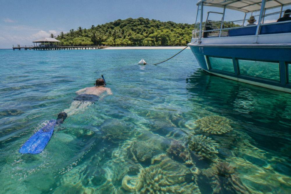 Snorkeller and glass bottom boat sharing the same shallow reef water above coral