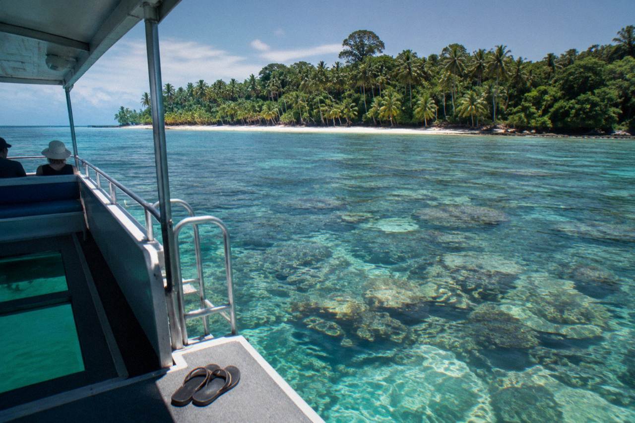 Glass bottom boat drifting over coral reef in clear turquoise water beside a tropical island