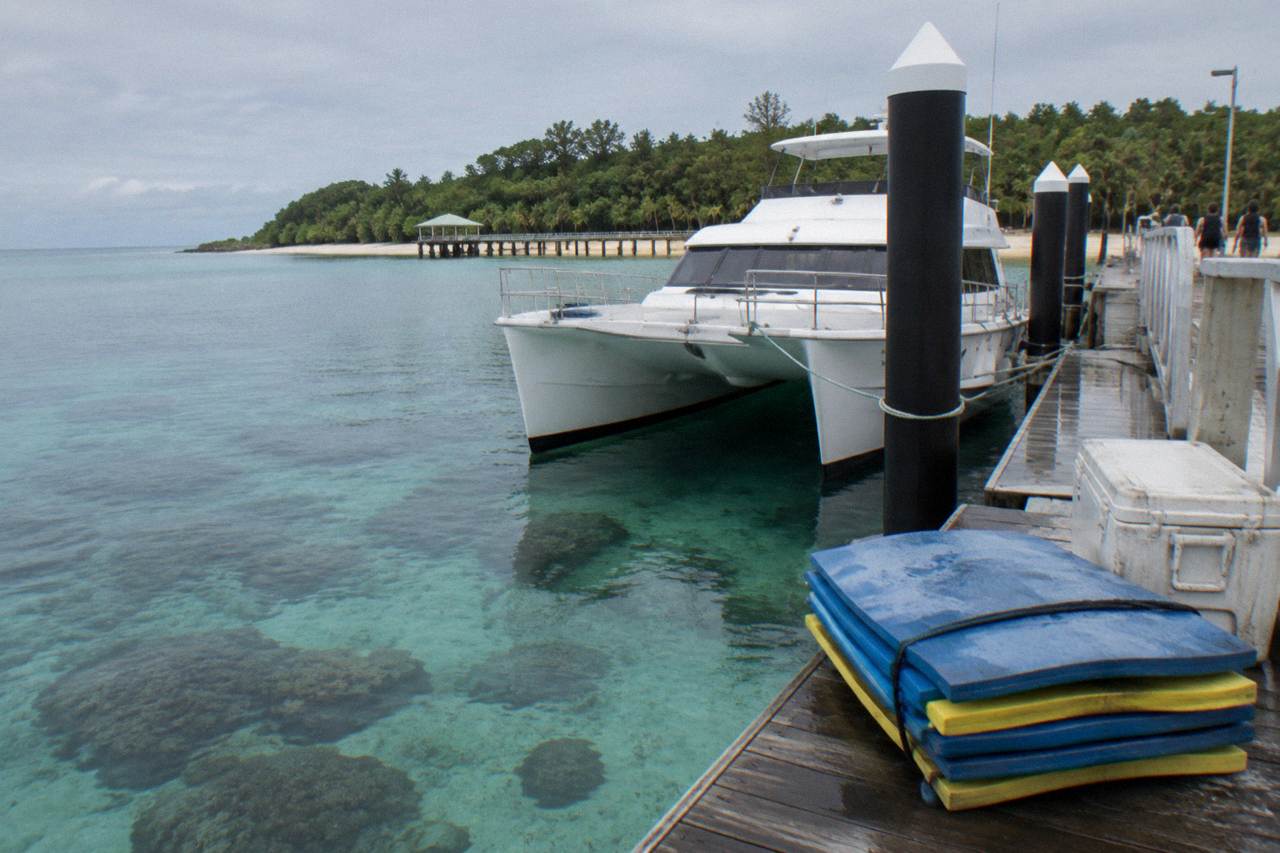 A catamaran moored at a tropical island jetty beside clear shallow reef water