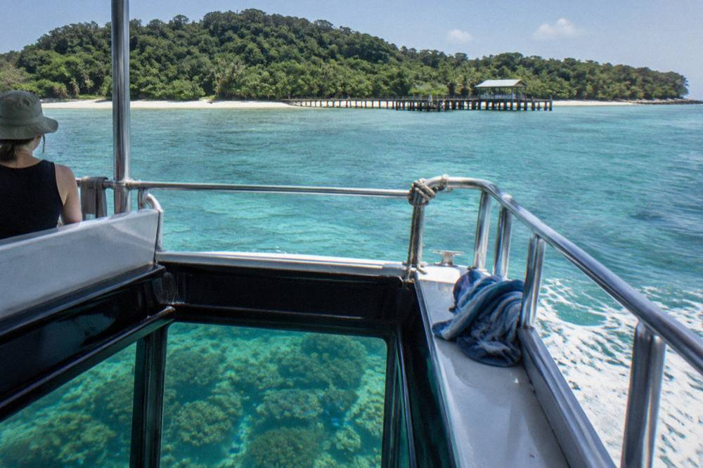 A glass-bottom boat drifting over coral bommies in shallow turquoise water