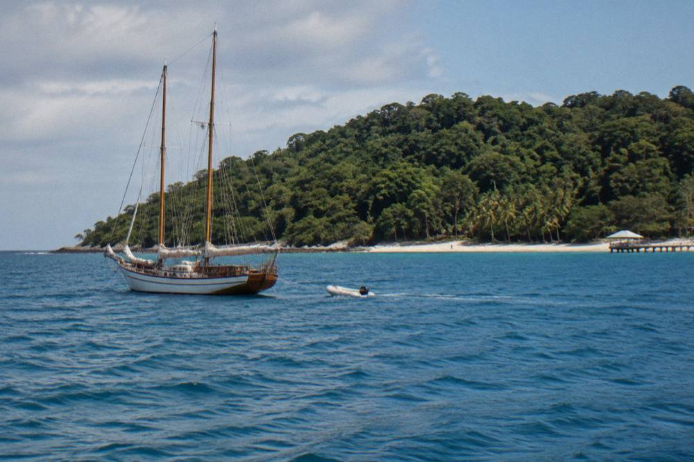 A small sailing schooner anchored off a green coral cay in calm blue sea