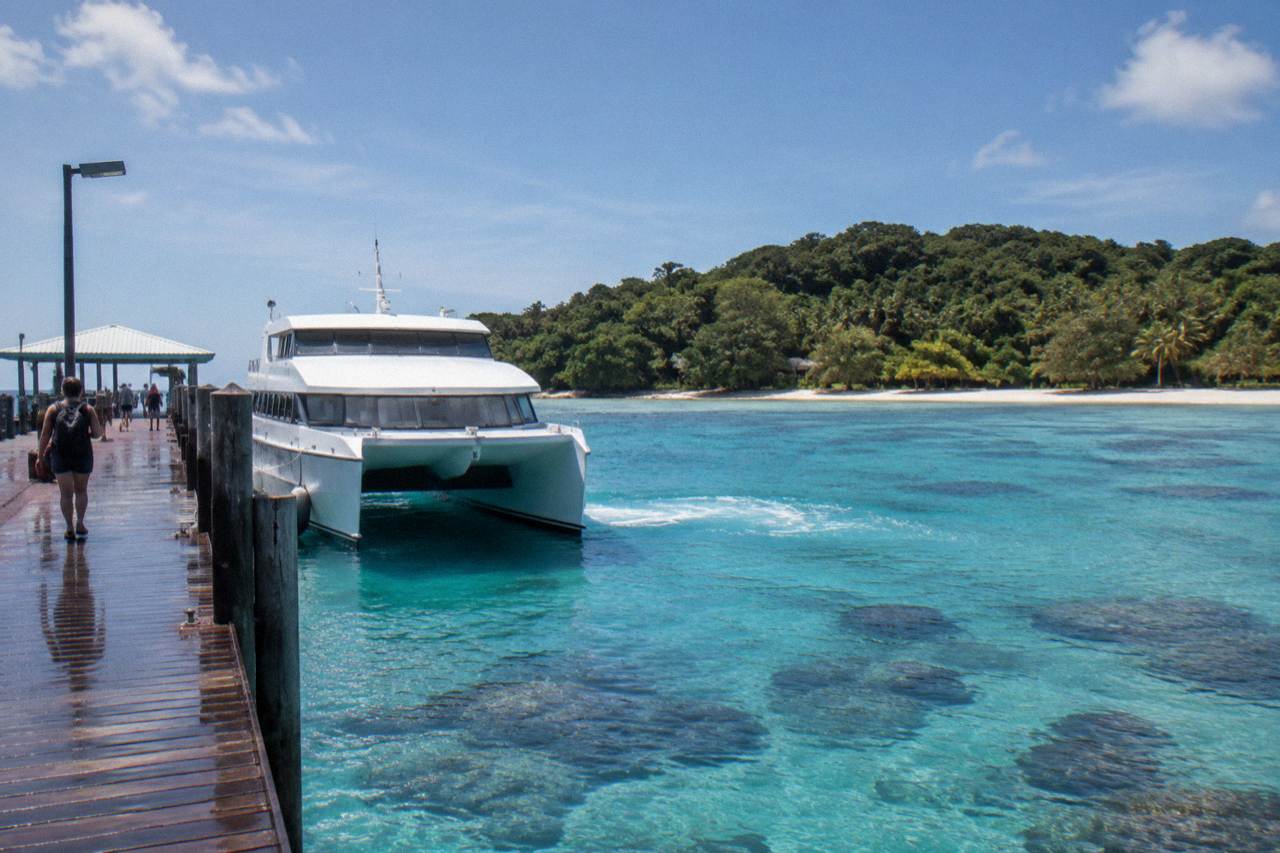 A fast catamaran moored at a tropical island jetty beside clear turquoise water