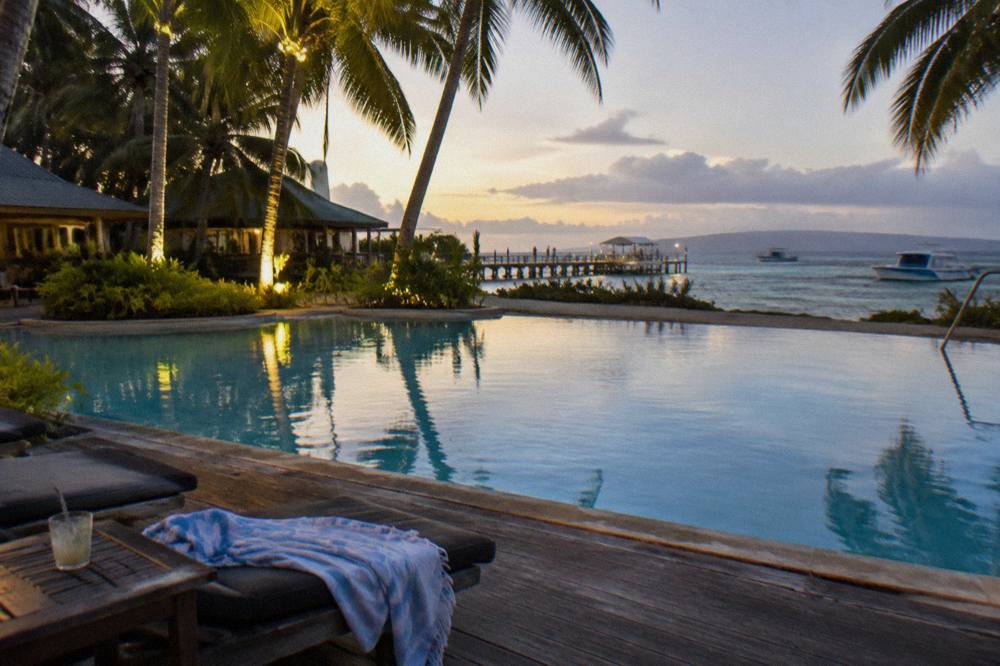 A resort swimming pool and timber deck looking out over calm reef water and moored boats