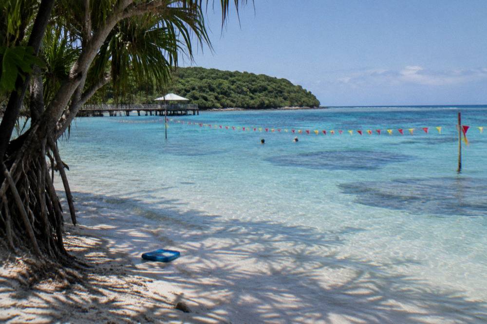 A calm patrolled swimming area with clear turquoise water over pale sand beside a tropical island shoreline