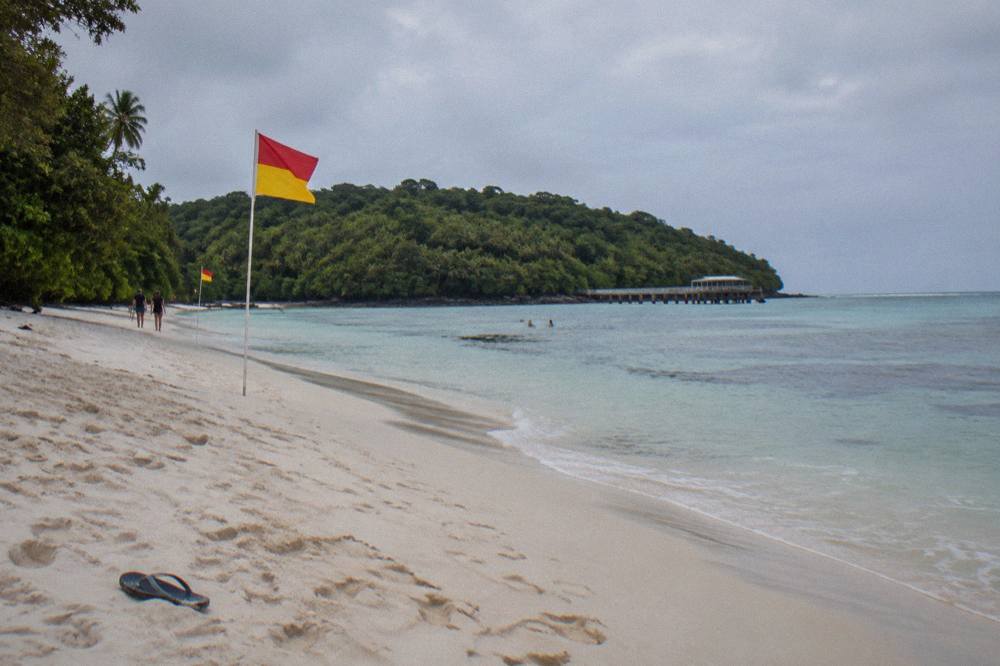 Patrolled swimming area with red and yellow flags on a tropical beach beside calm reef water