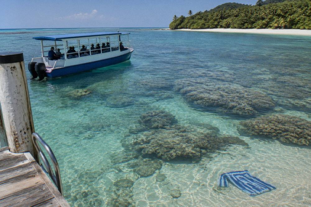 A glass-bottom boat drifting over coral reef in clear shallow water beside a tropical island