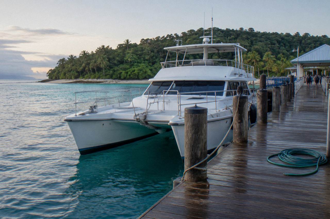 A catamaran moored beside a timber jetty at a green tropical island in calm blue water