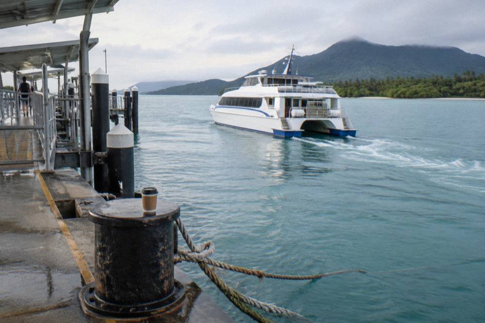 A fast catamaran ferry crossing calm blue water toward an island jetty