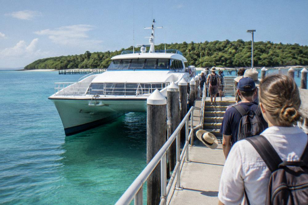A catamaran moored beside an island jetty with passengers walking down the pier