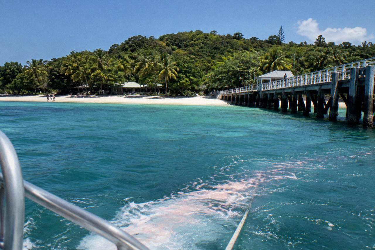 A sandy coral cay with turquoise shallows and a wooden jetty reaching into calm reef water