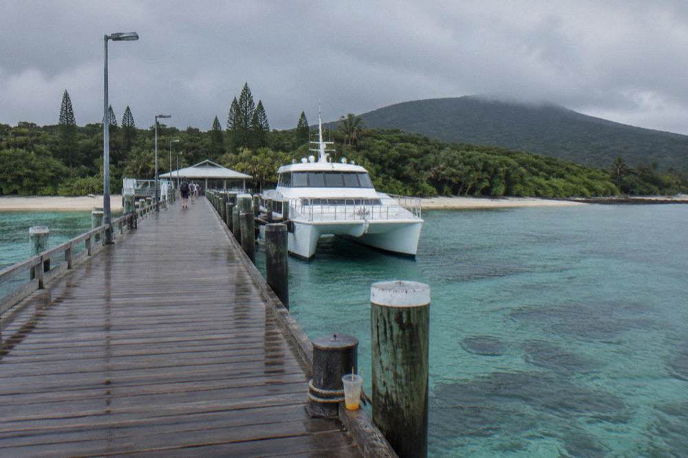A moored white catamaran at a timber jetty with clear shallow water on both sides