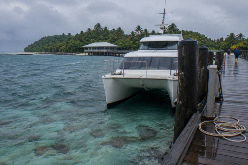 Catamaran moored beside a timber jetty above coral water