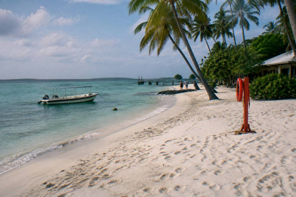 White sand beach with palm trees and a small day-boat moored in clear water nearby